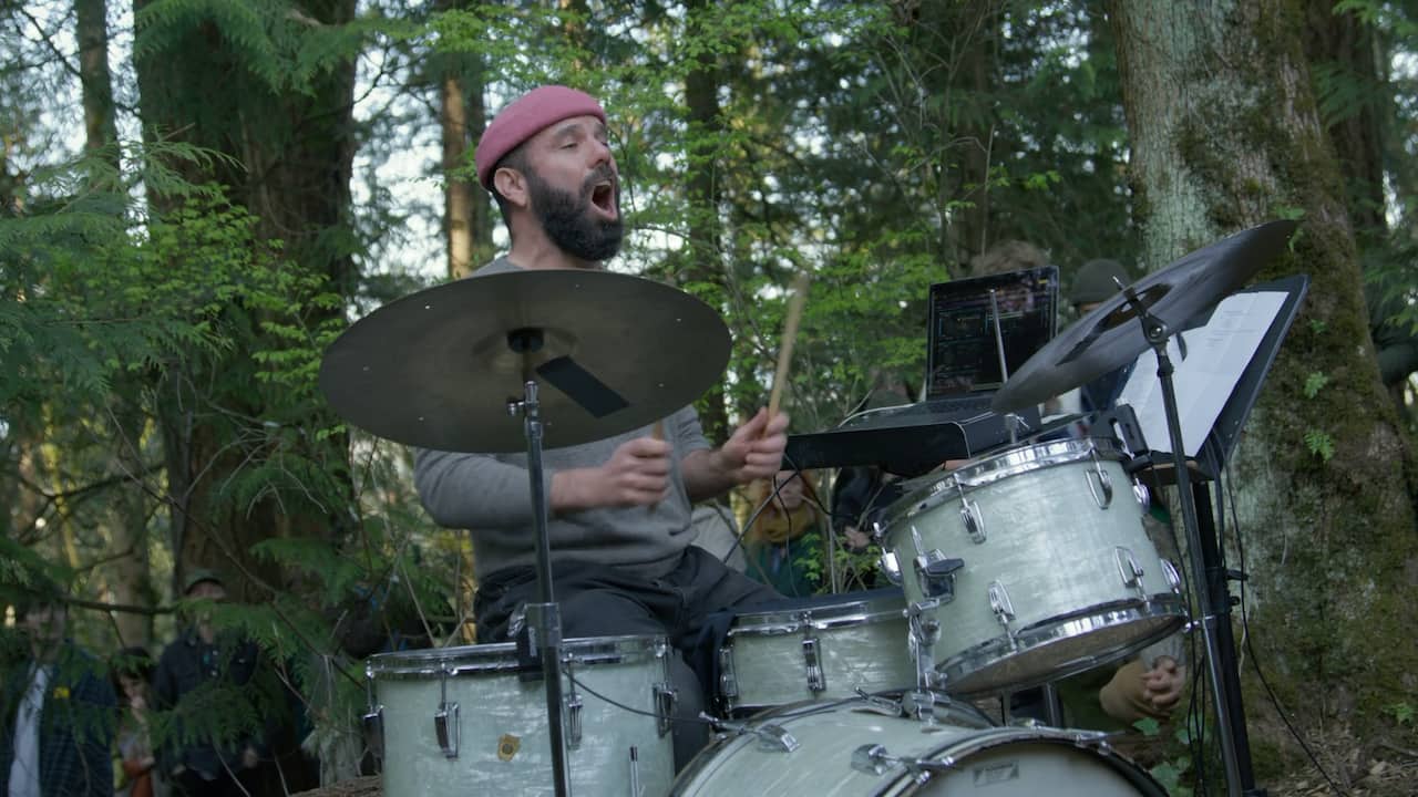 A photo of John Niekrasz playing drums in a forest.
