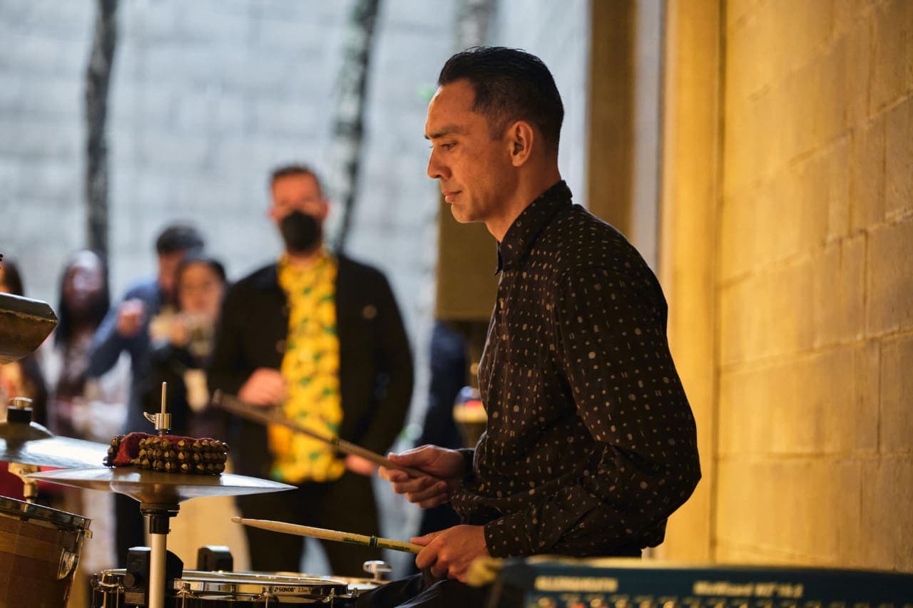 A side profile shot of Hashim at the drums with an audience in the background.