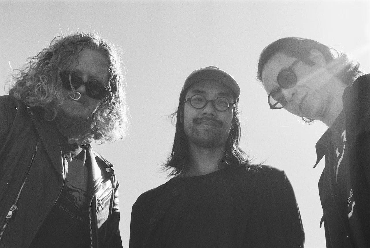 A black-and-white photo of Dave Harrington, Max Jaffe, and Patrick Shiorishi smiling and looking down at the camera.