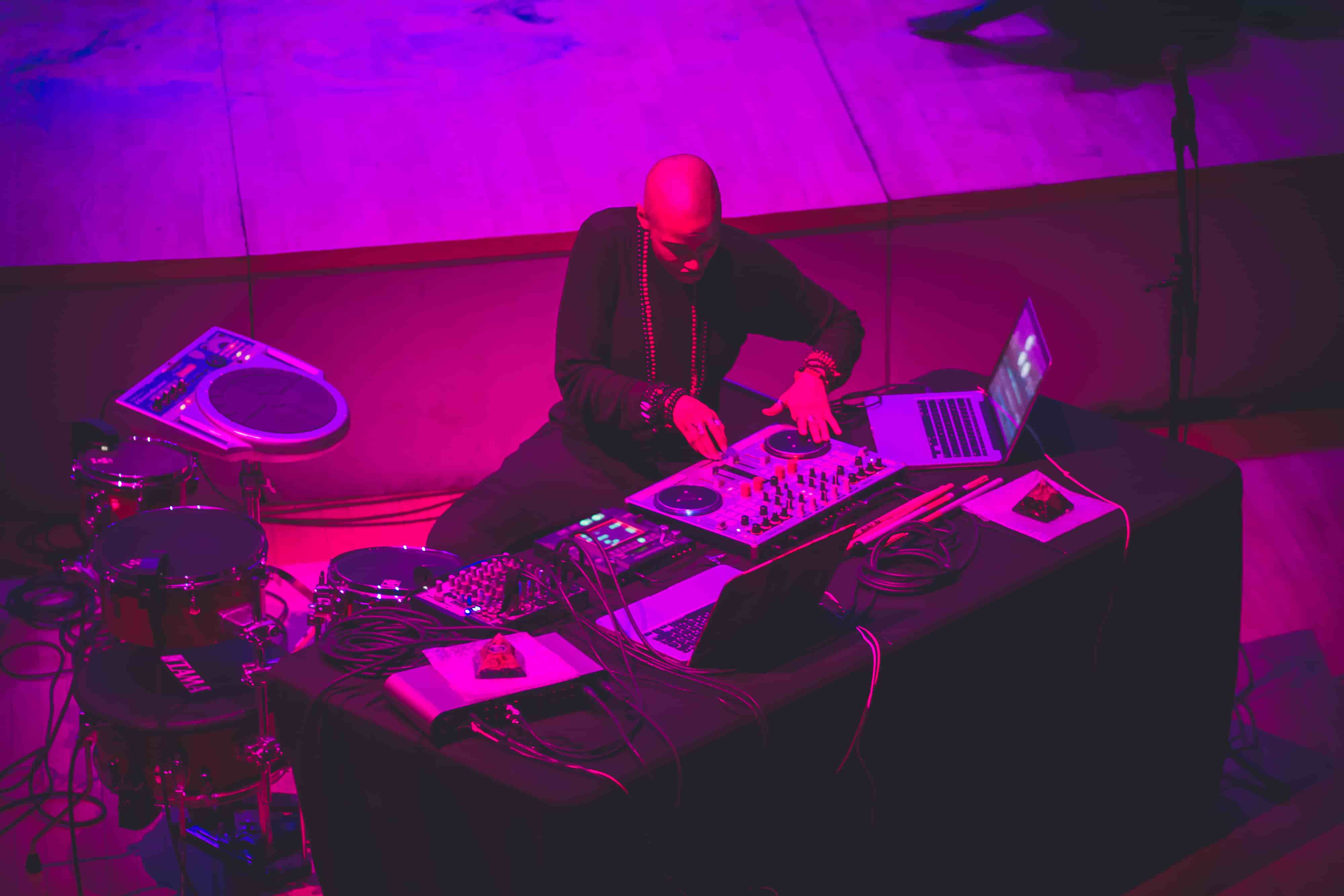 A photo of Val from above, surrounded by equipment: a Korg Wave Drum, a cocktail kit with Sensory Percussion, a turntable controller, and a computer. She's playing the turntable.