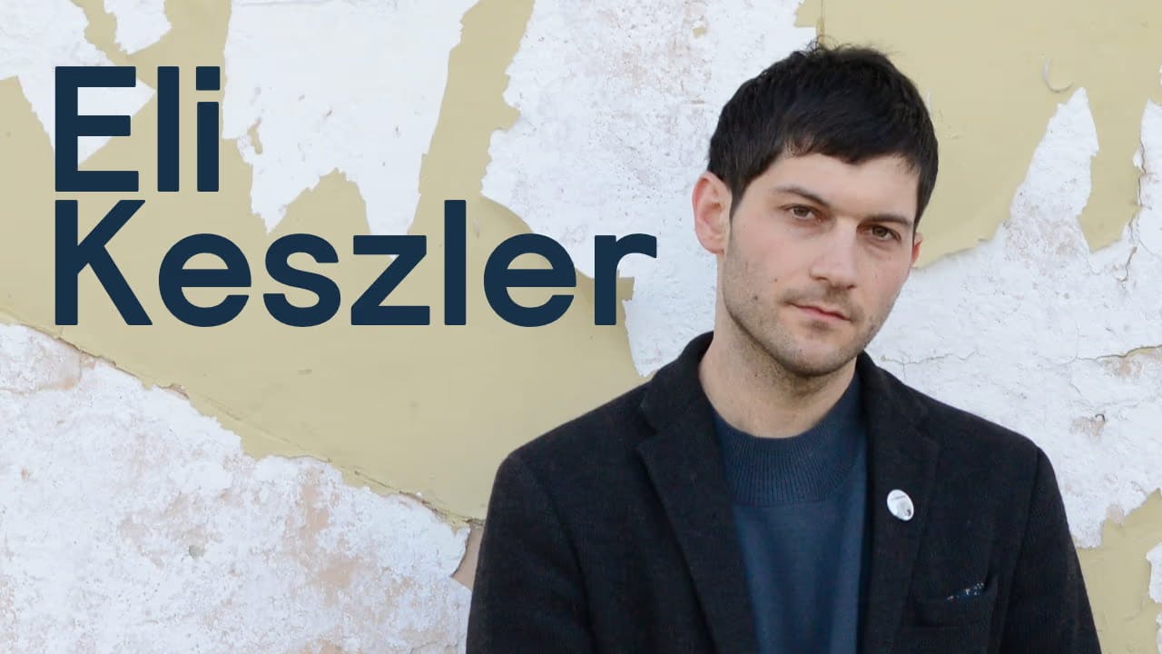 A photo of Eli Keszler standing in front of a wall