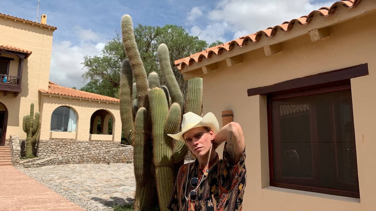 A photo of Mike Wallace wearing a cowboy hat standing in front of a large cactus